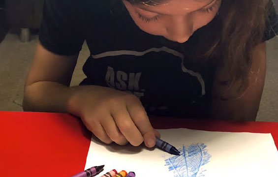Une enfant effectue le frottis d'une feuille à l'aide de crayons de cire.