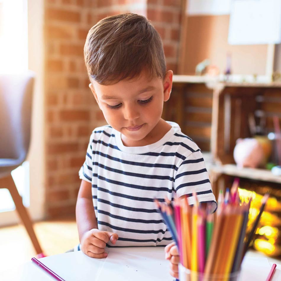 Un jeune enfant dessine avec des crayons de couleur.