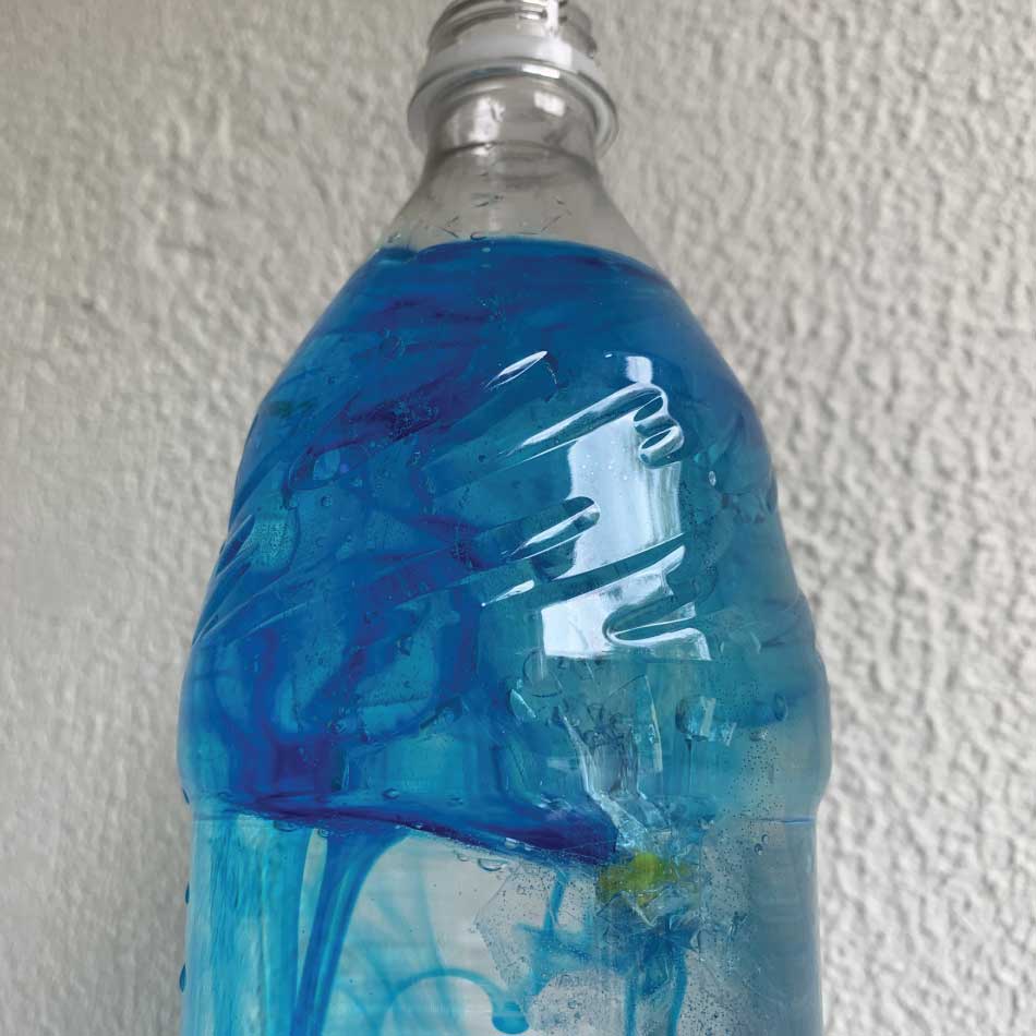 Une bouteille de plastique contenant de l'eau, un ballon de plastique et du colorant bleu.