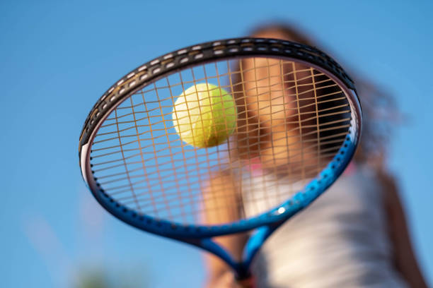 Une fille tient une balle de tennis en équilibre sur sa raquette.