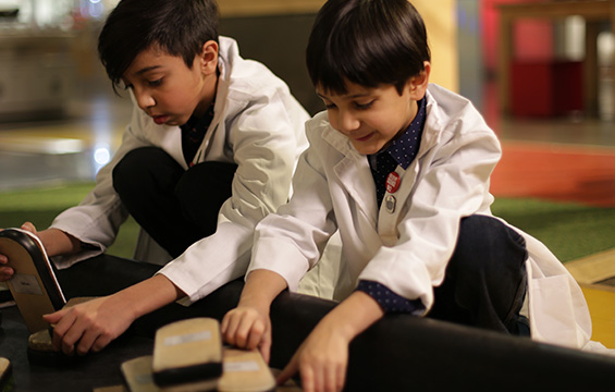 Deux garçons en sarrau font des expériences avec des blocs de friction au Centre des sciences.