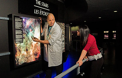 Un animateur présente un module d'exposition du Hall de l'Espace à une visiteuse.