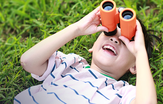 A young boy looks up at the sky with binoculars.