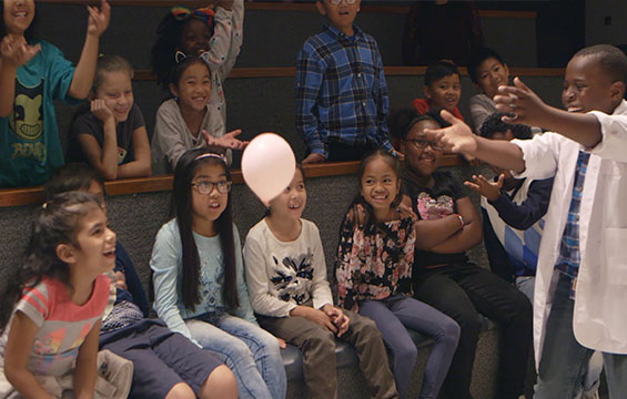 Dans un amphithéâtre, des élèves s'amusent à une leçon scientifique avec un ballon.