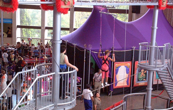 Une personne marche sur la corde raide devant des tentes évoquant le cirque.