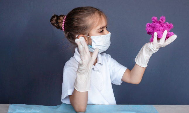 Une fille en habit protecteur tient un virus jouet.