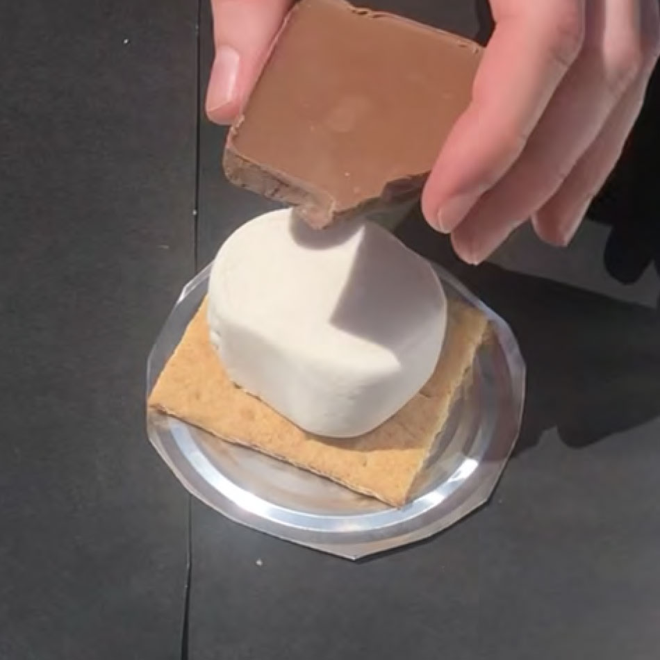 Une main assemble un s'more avec biscuit graham, guimauve et chocolat.