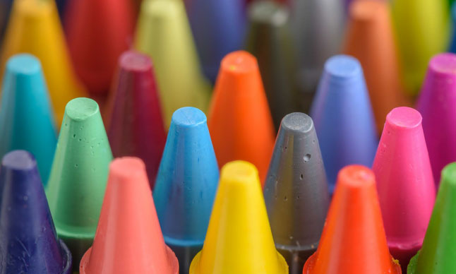 A close up of the tips of many different coloured crayons.