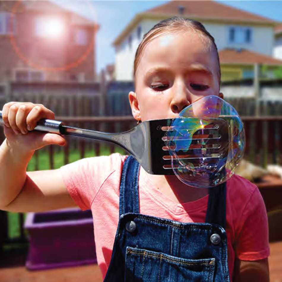 Une enfant souffle une grosse bulle au travers d'une spatule à égoutter.