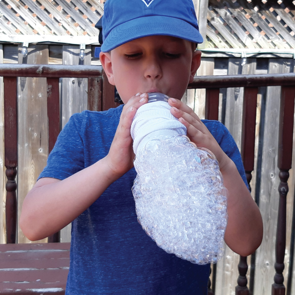 Un enfant souffle une multitude de bulles à travers une chaussette, formant une mousse.
