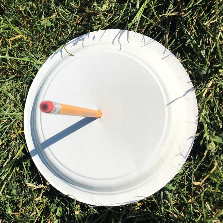 Un crayon à mine planté au milieu d'une assiette en carton projette son ombre sur l'assiette.