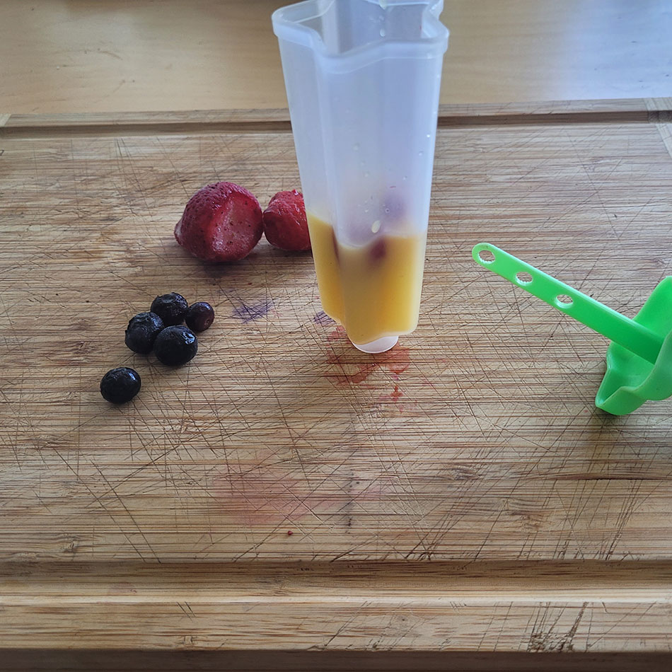 Des fruits à côté d'un moule à sucette partiellement rempli de liquide.