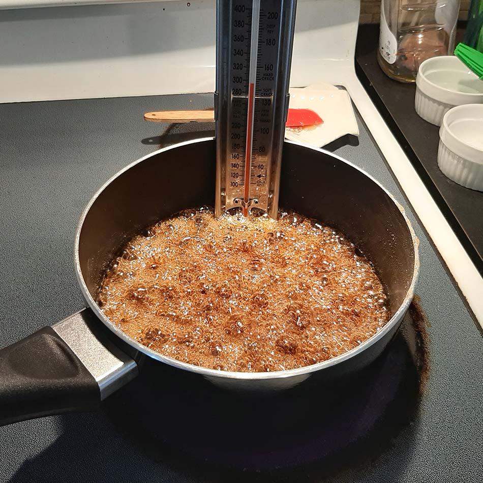 Un thermomètre à bonbons trempe dans une casserole de caramel bouillant.