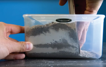 Close-up of hands manipulating layers of dirt in a plastic container.