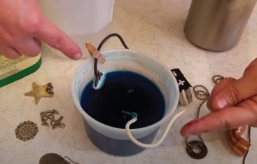 Two electrodes sit in dark-coloured liquid in a plastic cup.