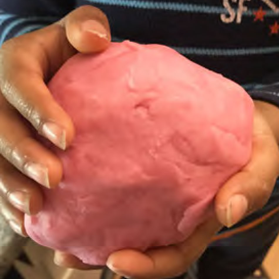 Des mains d'enfant tiennent une boule de pâte à modeler maison.