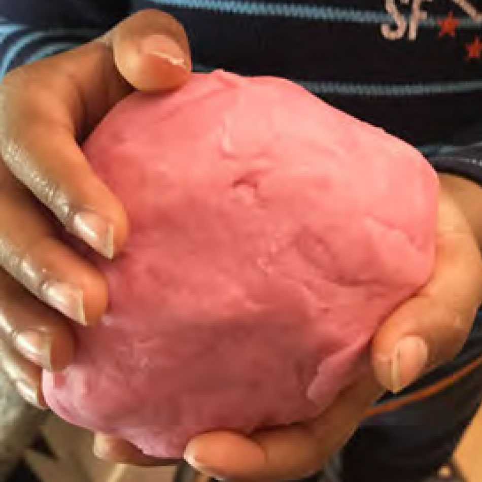Des mains d'enfant tiennent une boule de pâte à modeler maison.