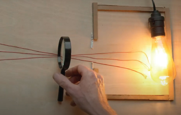 A hand hold a magnifying glass in front of a light bulb.