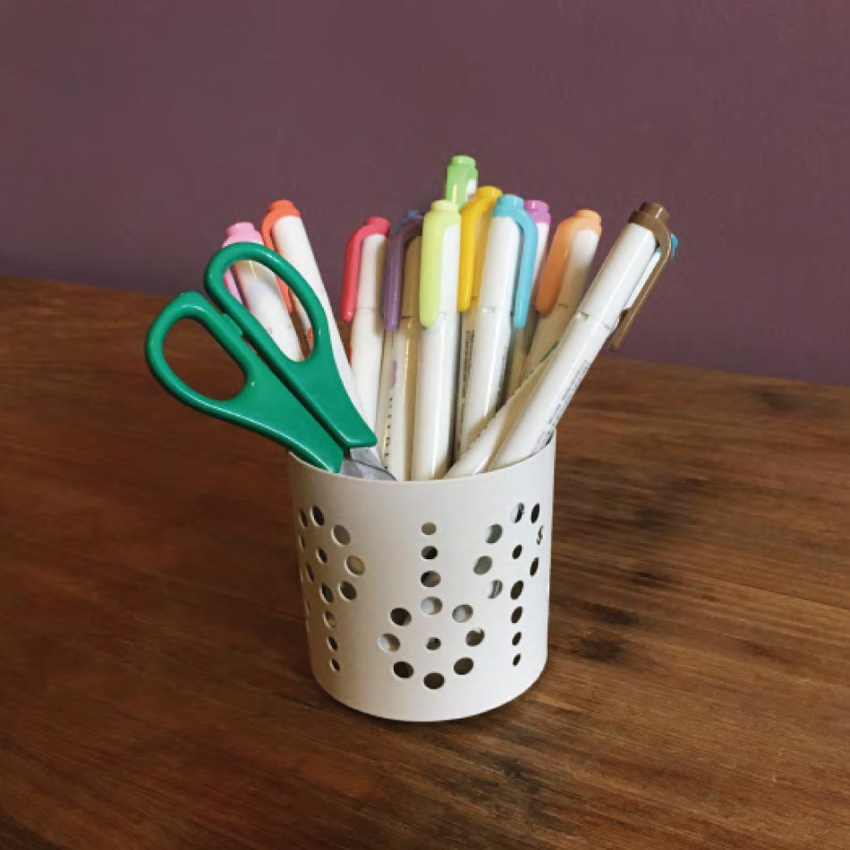Un porte-crayon posé sur une table contenant plusieurs marqueurs multicolores et une parie de ciseaux.