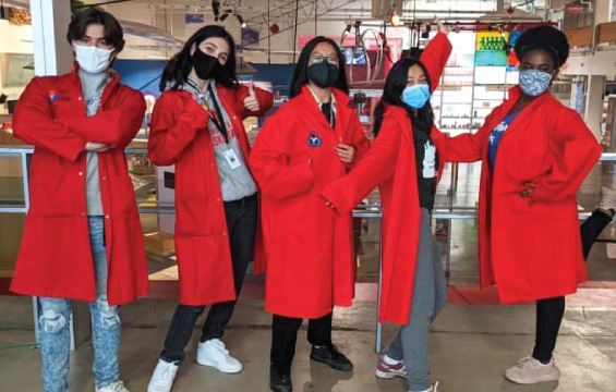 Un groupe d'élèves de l'école des sciences en sarraus rouges posent devant un hall d'exposition.