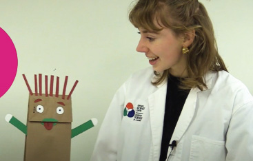 An educator speaks with a paper bag puppet with red spiky hair.