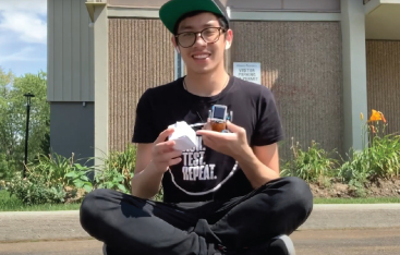 An educator sit on the ground outside, holding a paper cube and a small toy car.