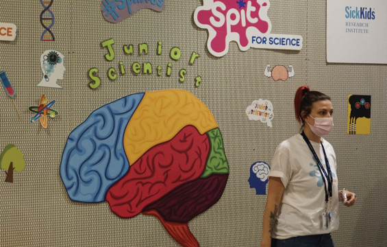 Une chercheuse de SickKids debout devant un mur couvert d'illustrations scientifiques, dont des schémas de cerveaux.