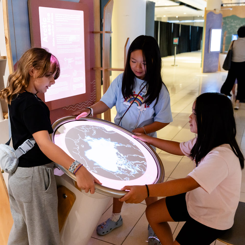 Un groupe de trois filles font tourner la carte pour voir comment les saisons changent partout dans le monde.