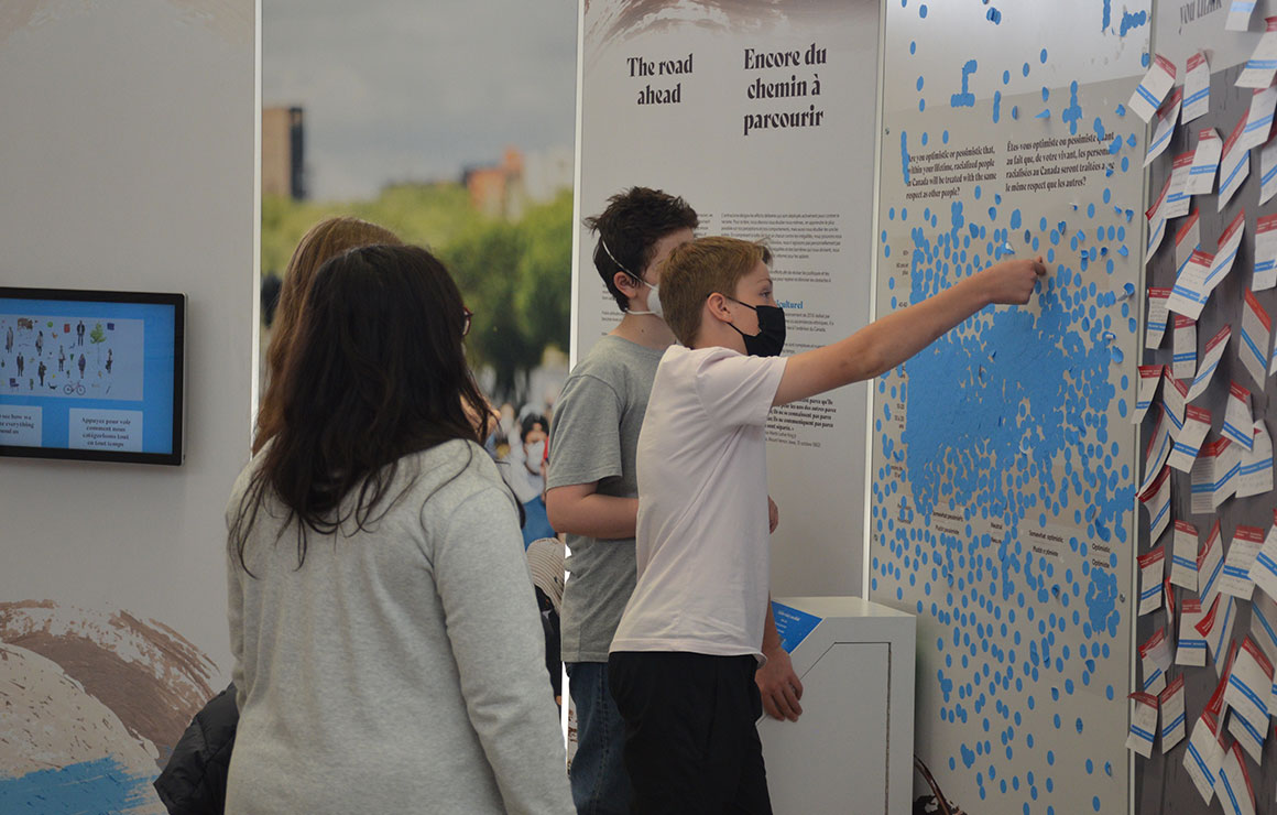 Quelques personnes posent des autocollants sur un panneau de l'exposition.