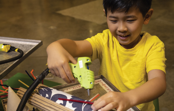 Un jeune enfant bricole avec du carton et un pistolet à colle.