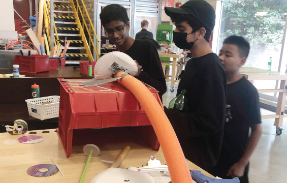 Trois élèvent élaborent une machine Rube Goldberg dans un atelier.