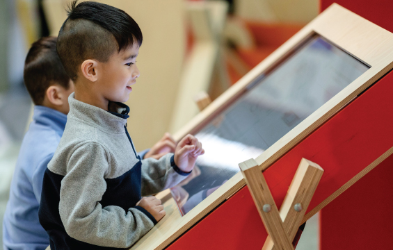Deux enfants interagissent devant un écran tactile géant.
