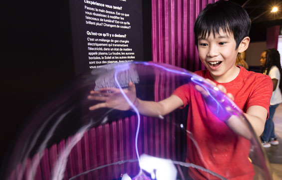 Un garçons posant les mains sur une boule de plasma.