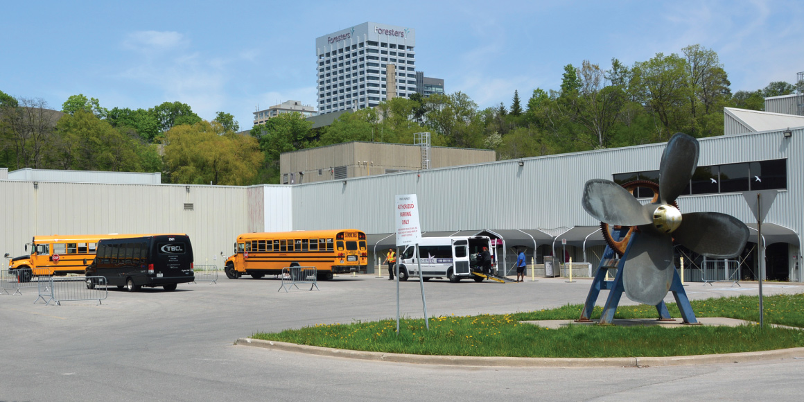 The rear entrance of the Science Centre with two school buses and two shuttle buses out front. The propeller sculpture is also visible.