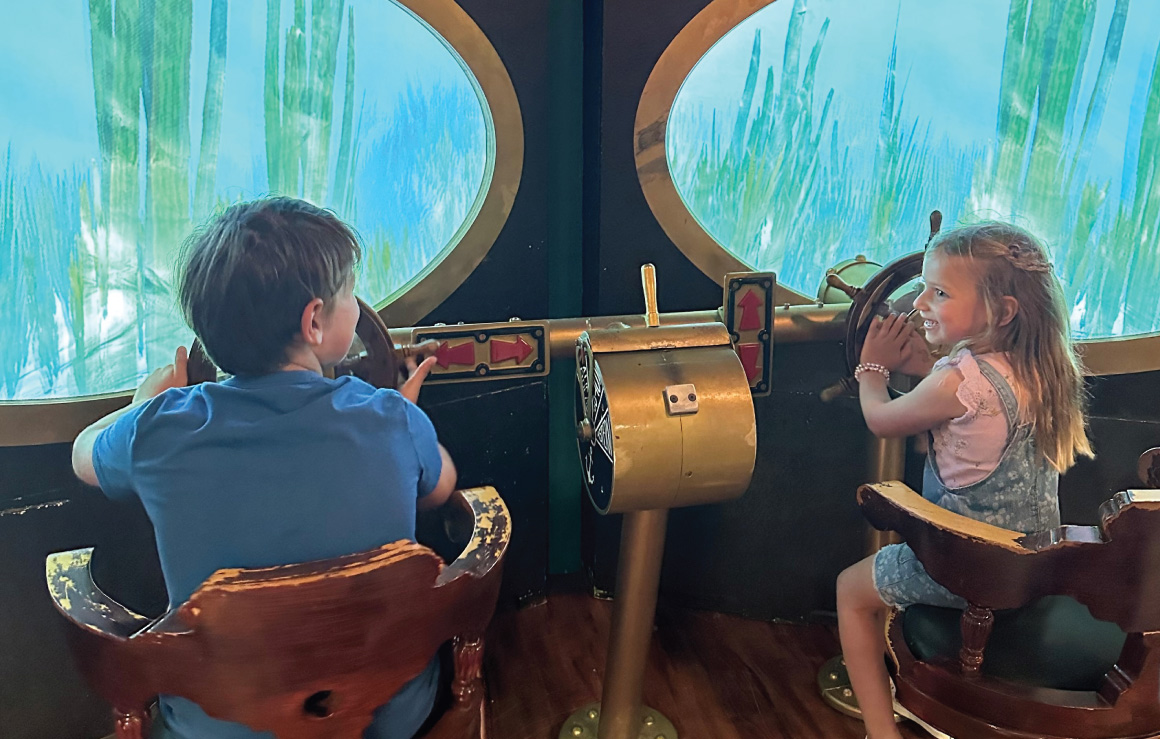 Deux enfants assis à la barre du Nautilus, les mains aux gouvernails.