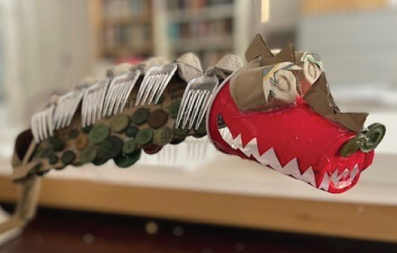 Un dinosaure fabriqué à partir de fourchettes en plastique, de boutons, de boîtes à œufs et d'un gobelet rouge, entre autres matériaux.