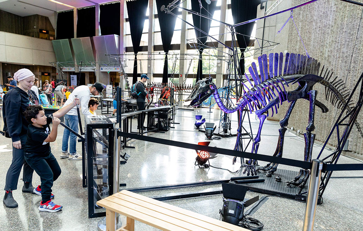 Des gens actionnent une sculpture de dinosaure en métal.