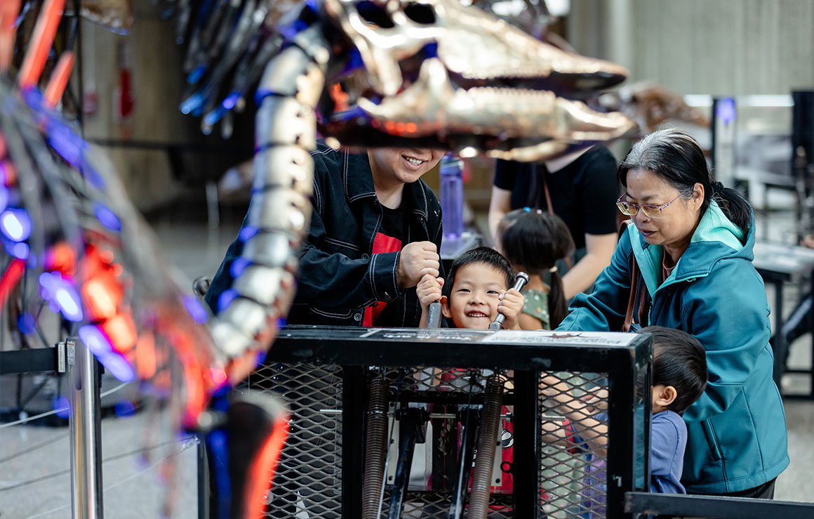 Des gens actionnent une sculpture de dinosaure en métal.
