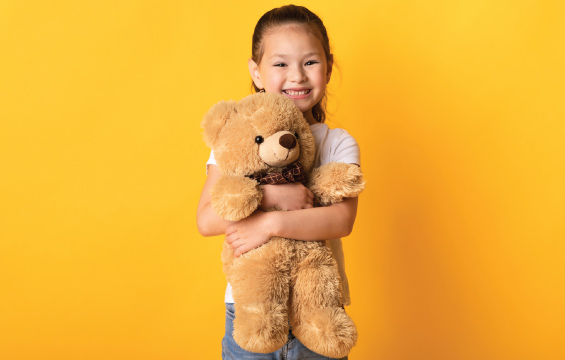 Une enfant serre un ourson en peluche en souriant.