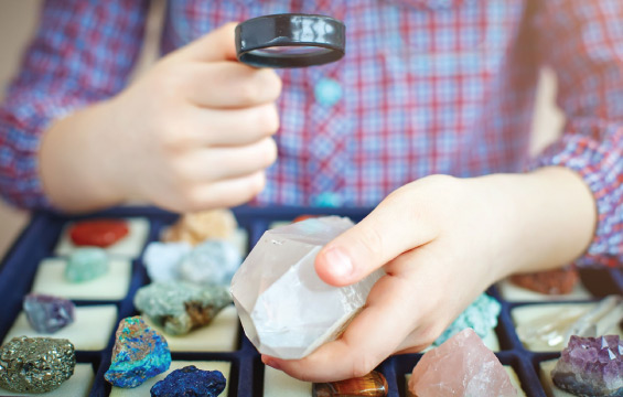 Un enfant examine à la loupe une colletion de roches et de minéraux.