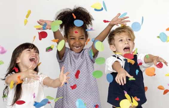 Trois enfants souriants lancent des confettis.