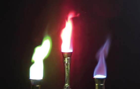 Trois becs brûleurs allumés présentant trois flammes différentes : verte, rouge et violette.