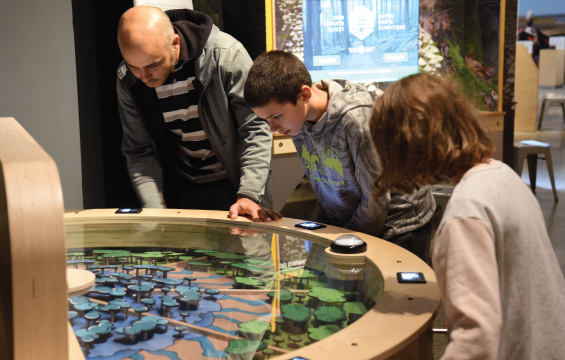 Un homme et deux enfants manipulent un module de l'exposition Notre Quête climatique.