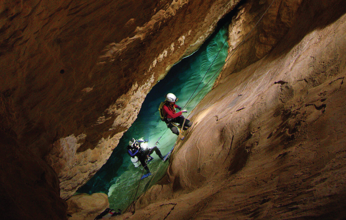 Deux scientifiques gravissent une paroi rocheuse pour sortir de l'eau d'une grotte.