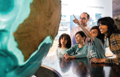 Deux adultes et trois enfants examinent un énorme globe terrestre.