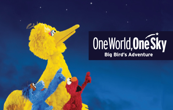 Les muppets Big Bird et ses deux amis pointent le ciel de nuit devant un enseigne disant : «One World, One Sky, Big Bird's Adventure».