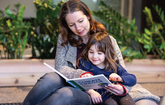 Une femme lit un livre appelé «Climate Change», une enfant assise sur ses genoux.