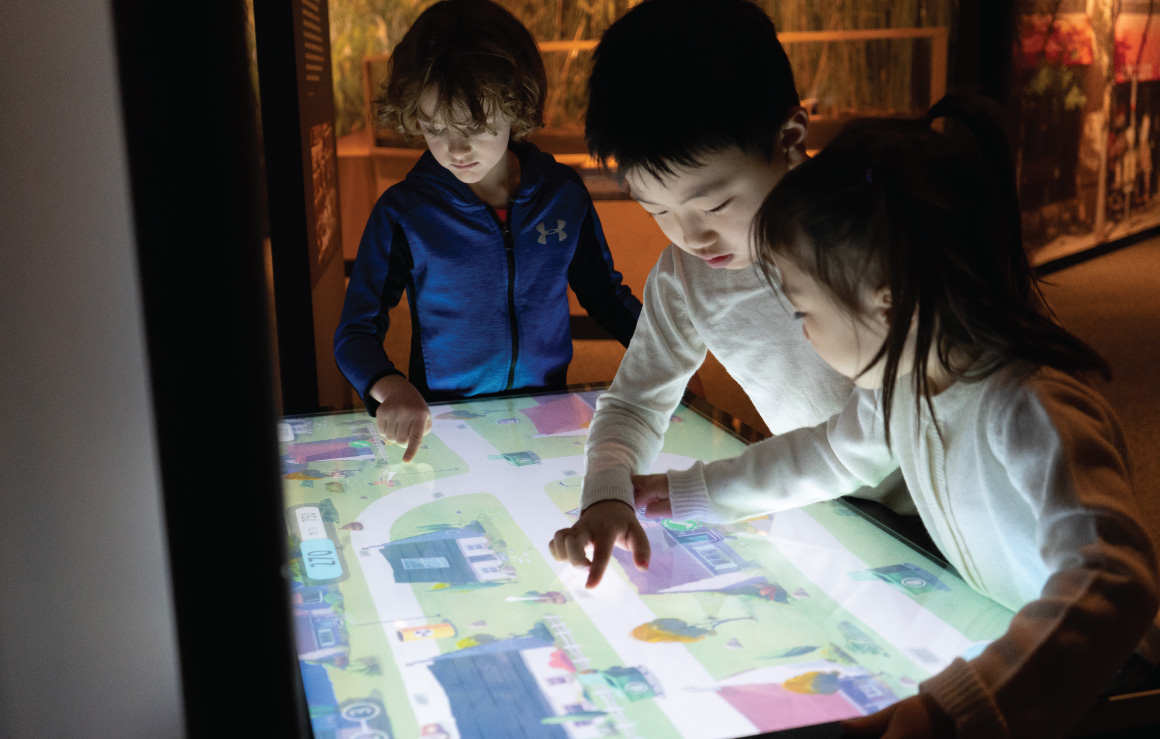 Trois enfants interagissent avec un écran tactile.