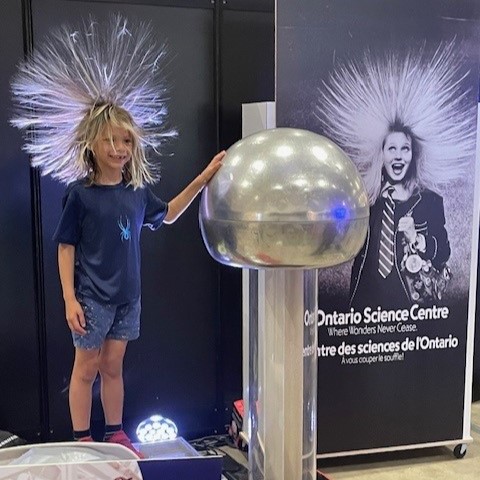Une enfant a les cheveux dressés sur sa tête en touchant le générateur de Van de Graaff du Centre des sciences de l'Ontario.