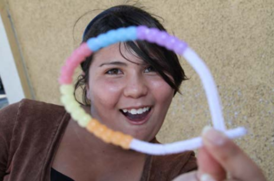 Une fille souriante présente un bracelet de perles UV au premier plan.